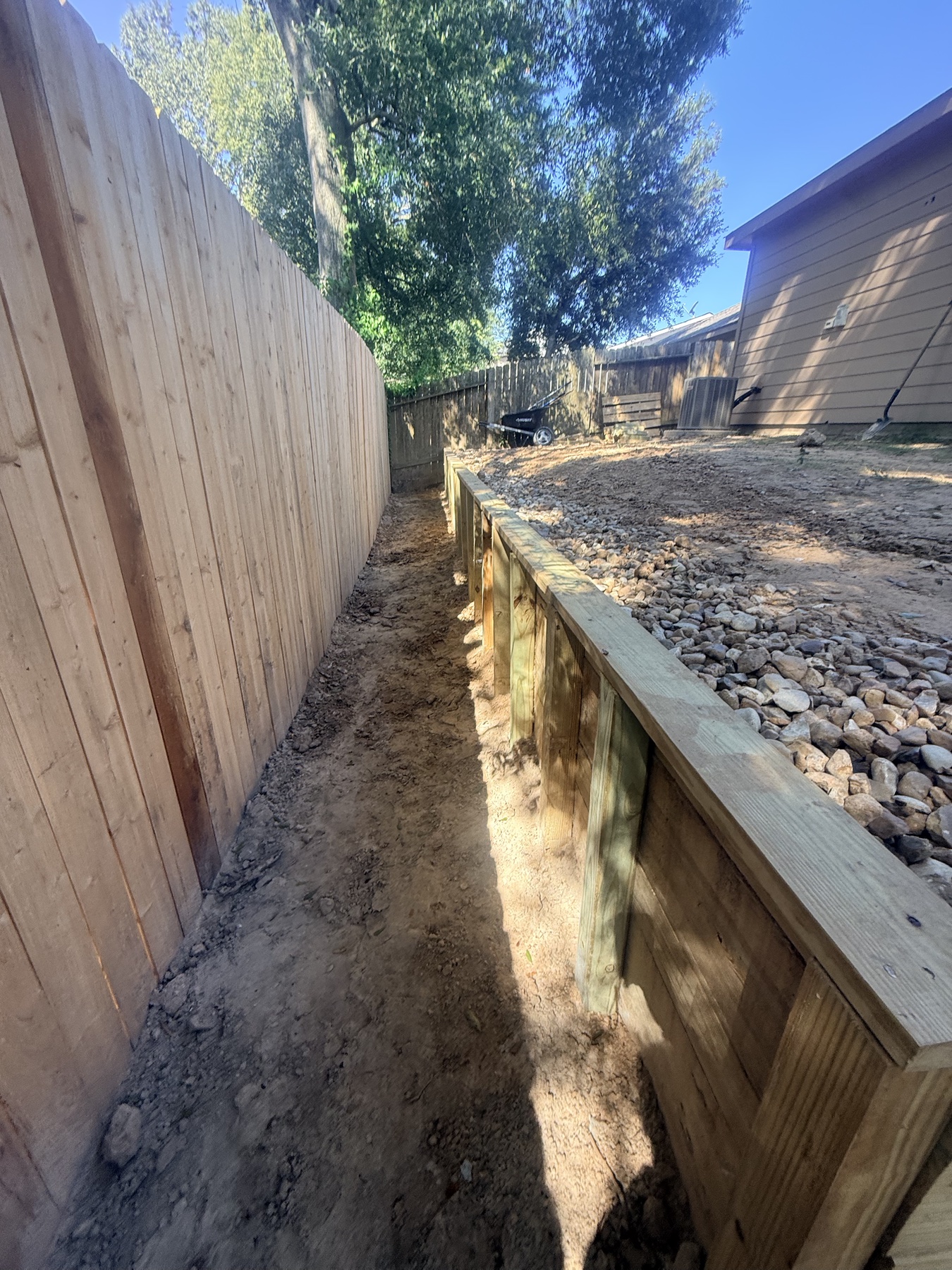 Completed timber retaining wall, gravel drainage edge, and cedar privacy fence at the Conroe garden
