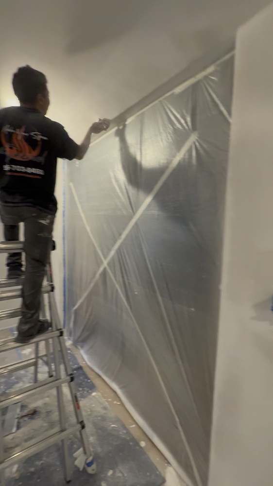 Sacred Innovations crew member working beside a protective plastic barrier in the living room